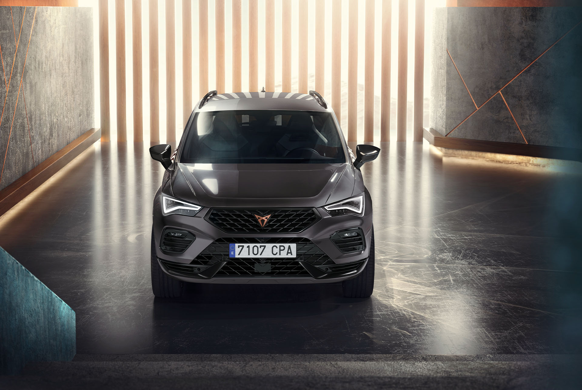 Vue avant du Cupra Ateca, un SUV gris, dans un cadre moderne et éclairé. La calandre audacieuse, les phares LED et le design épuré de la voiture sont mis en évidence. 