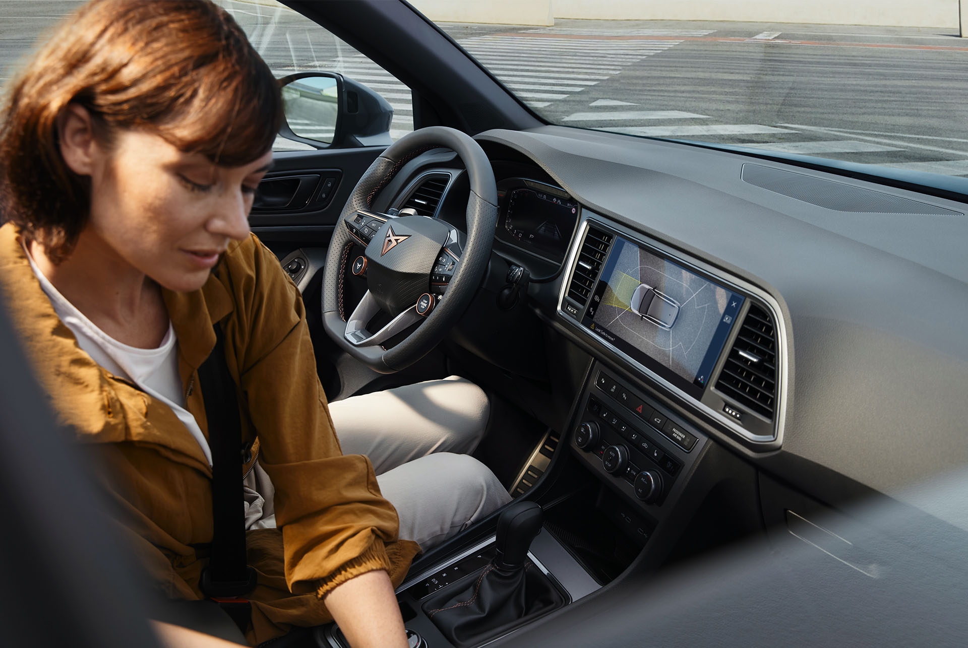 Intérieur de la cupra ateca mettant en avant les caractéristiques technologiques avancées. Le tableau de bord affiche un grand écran d’infotainment avec navigation et le volant avec boutons satellites aux commandes intégrées. Une femme se trouve dans l’habitacle. 