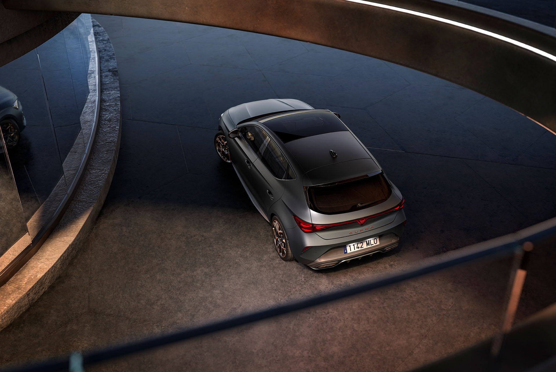 Technologie de la nouvelle Cupra Leon 2024 hybride, éclairage LED arrière, véhicule PHEV garé sur le ciment, structure avec des bords lumineux. Le véhicule est présenté dans une finition Gris mat avec des jantes forgées en Cuivre et Noir.