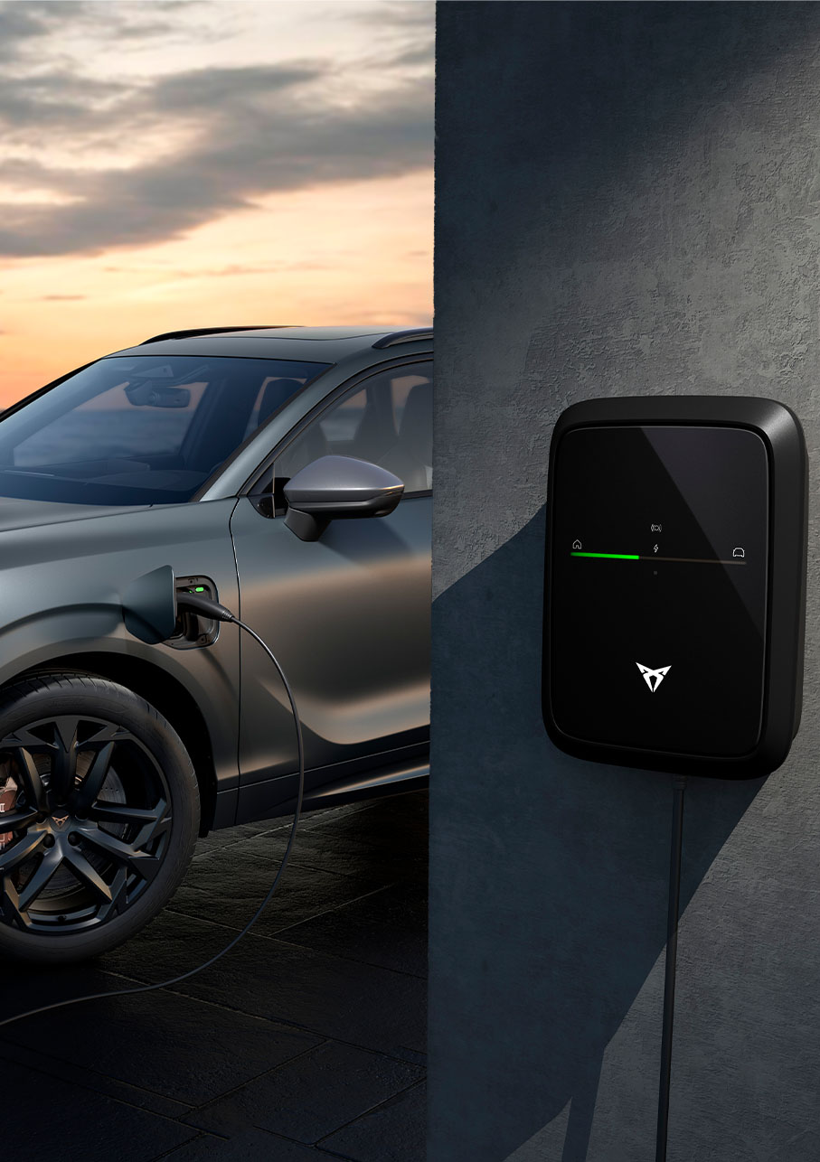 nouveau véhicule hybride rechargeable cupra terramar en charge, version exclusive america’s cup, couleur gris encelade mat, avec jantes en alliage de 20 pouces america’s cup, devant le coucher du soleil en bord de mer.