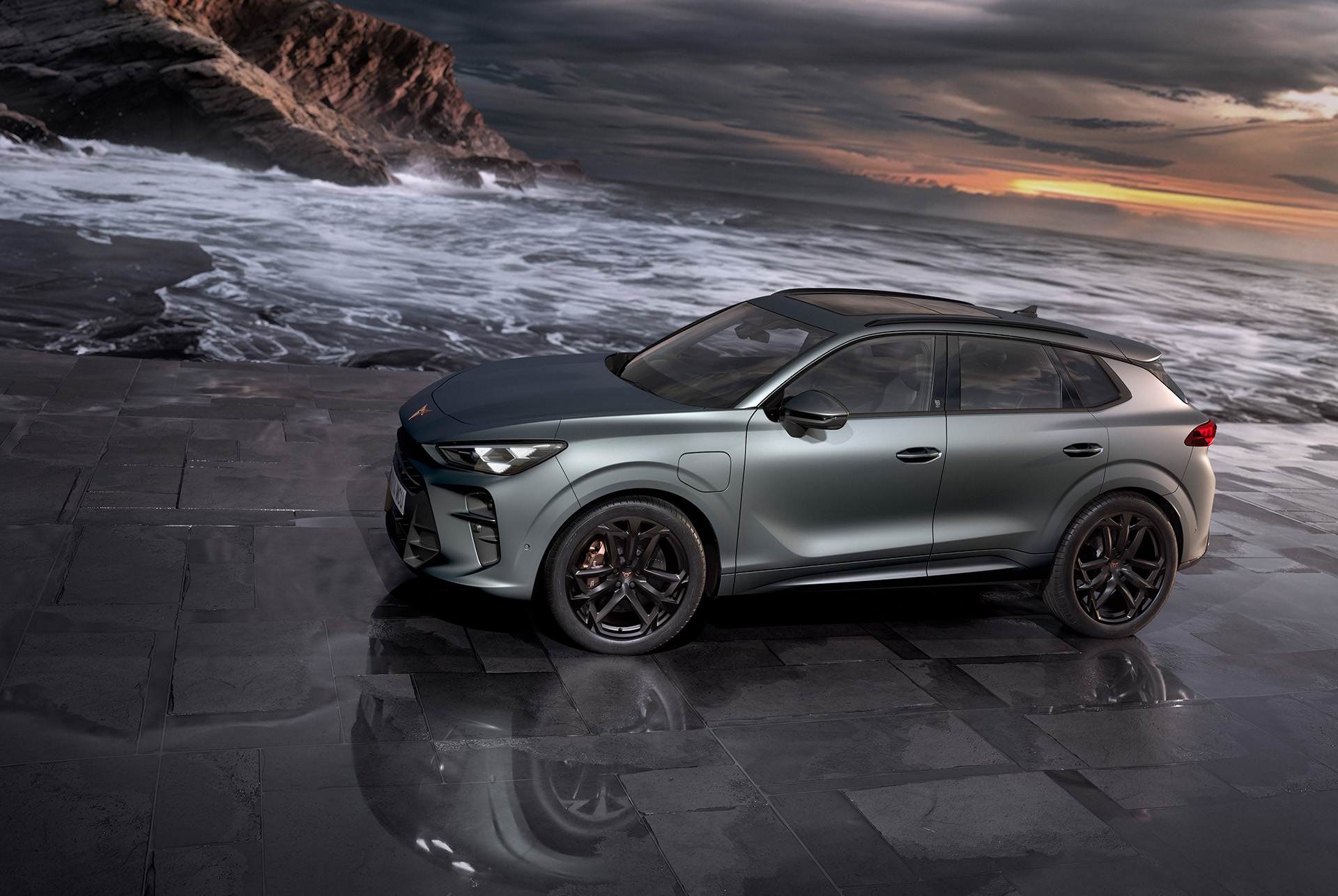 suv hybride cupra terramar, nouveau modèle 2024, vue latérale, équipé de jantes en alliage de 20 pouces america’s cup et de freins akebono, gris encelade mat, sur une chaussée mouillée devant le coucher du soleil en bord de mer. 