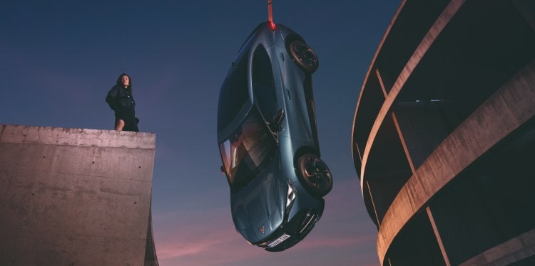 Cupra Tavascan suspendu à un cadre en béton avec le ciel en toile de fond et un modèle.